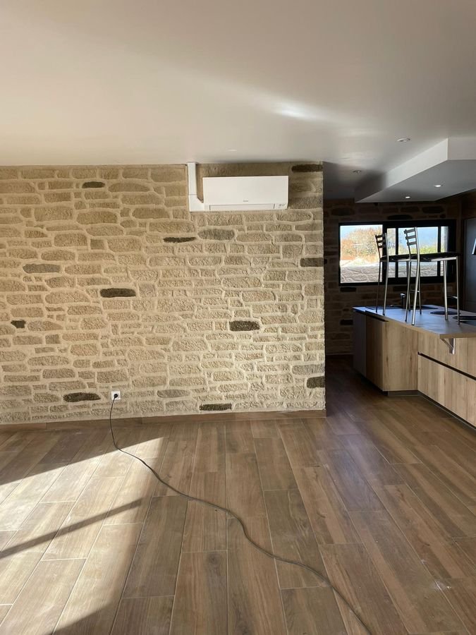 Séjour livré par Soly'bat : mur en pierre apparente, climatiseur mural, cuisine ouverte au fond